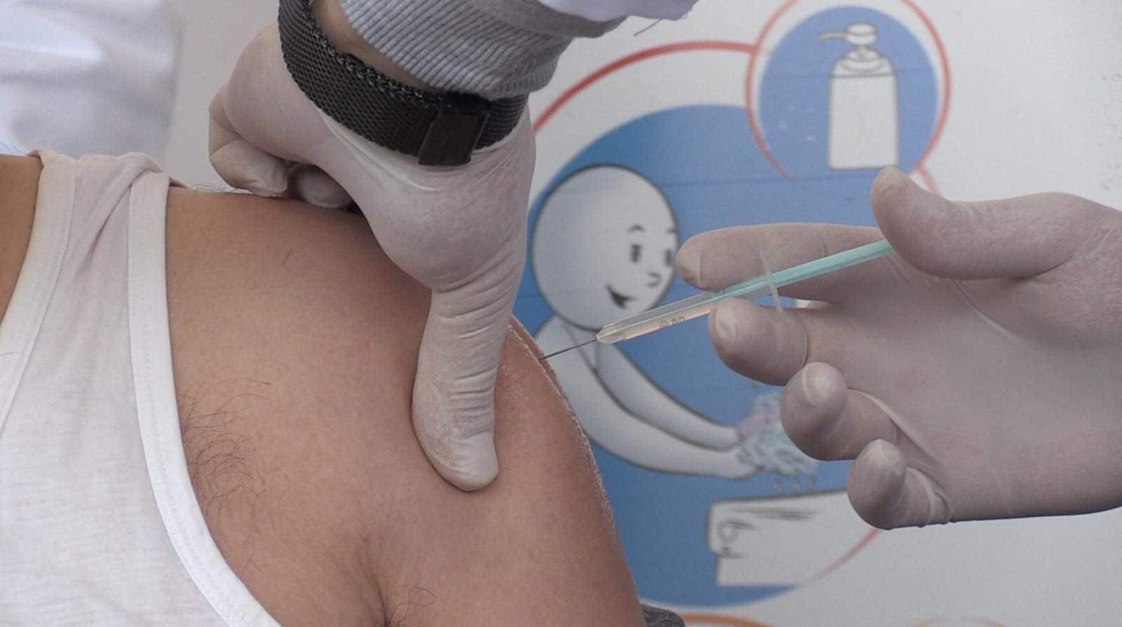 Un bărbat e vaccinat anti-covid-19. Acesta poartă un maiou alb.