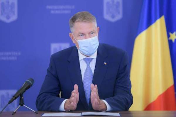 Klaus Iohannis vorbește în cadrul unei conferințe, îmbrăcat în costum albastru, gesticulează și poartă masca de protecție