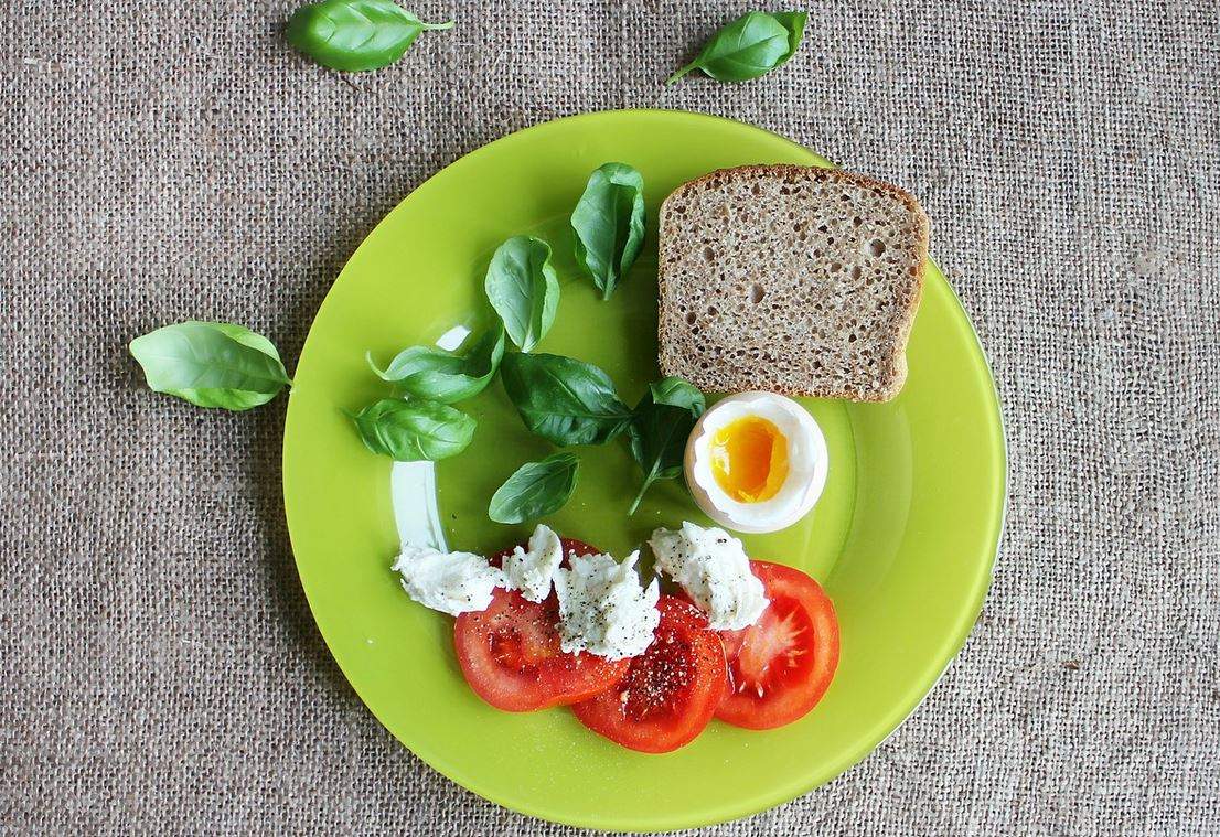 Un mic dejun cu ou, roșii, pâine neagră și spanac. Ingredientele sunt pe o farfurie verde.
