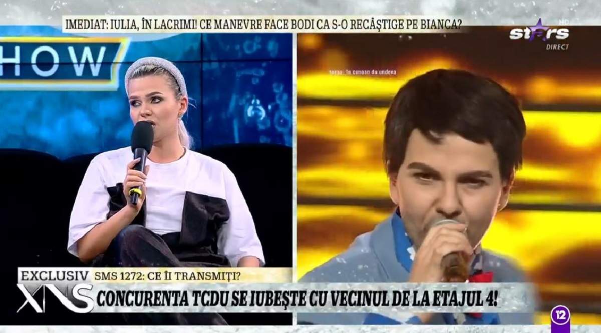 Cristina Vasiu e pe canapea la Xtra Night Show. Vedeta vorbește la microfon și poartă un tricou alb și o salopetă neagră.
