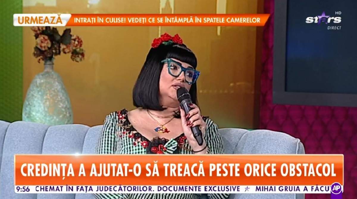Ozana Barabancea poartă o rochie în dungi albe și negre și o coroniță cu flori roșii pe cap. Vedeta vorbește la microfon, la Antena Stars.