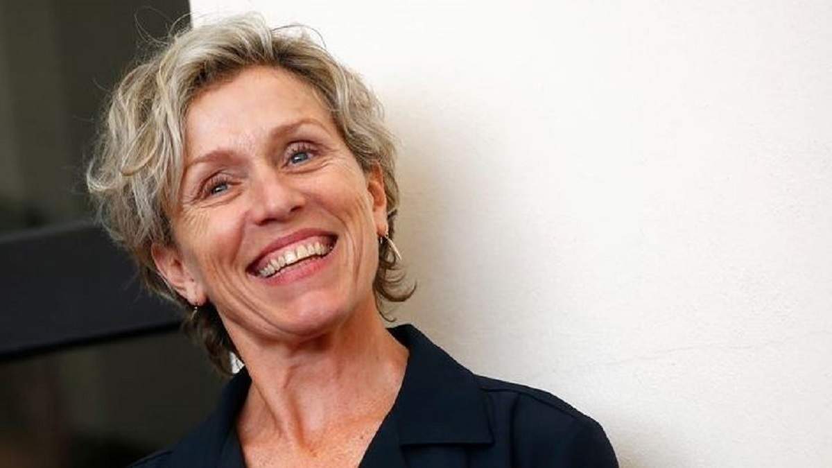 Frances McDormand poartă un sacou negru. Artista zâmbește larg.