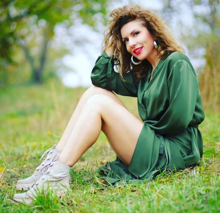 Carmen Brumă stă pe iarbă și poartă o rochie verde. Vedeta își ține o mână prin păr și are în picioare bocanci gri.