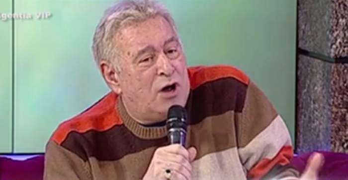 Marian Voicu poartă un pulover colorat în dungi mari, albe, maro și portocalii. Politicianul vorbește la microfon.