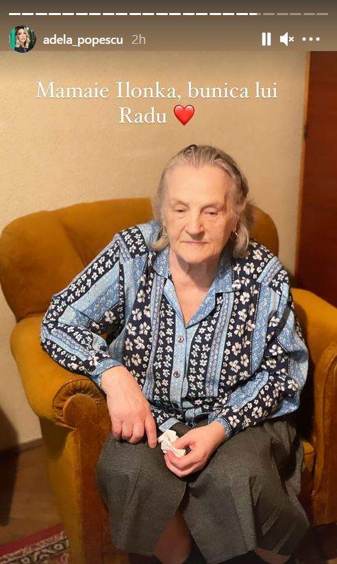 Ilonka, bunica lui Radu Vâlcan, stă un fotoliu maro. Aceasta poartă o fustă gri și o cămașă colorată în nuanțe de bleu și negru, cu floricele.