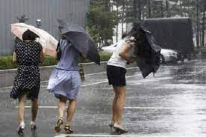 Trei femei care aleargă prin ploaie cu umbrele în mâini