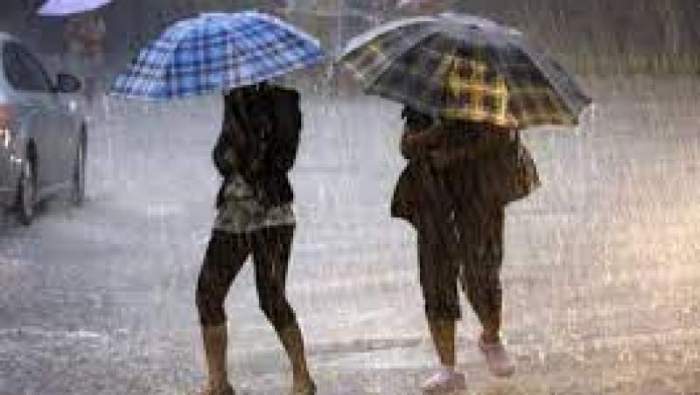 Doi femeie pe stradă, prin ploaie, cu umbrele deschise în mână
