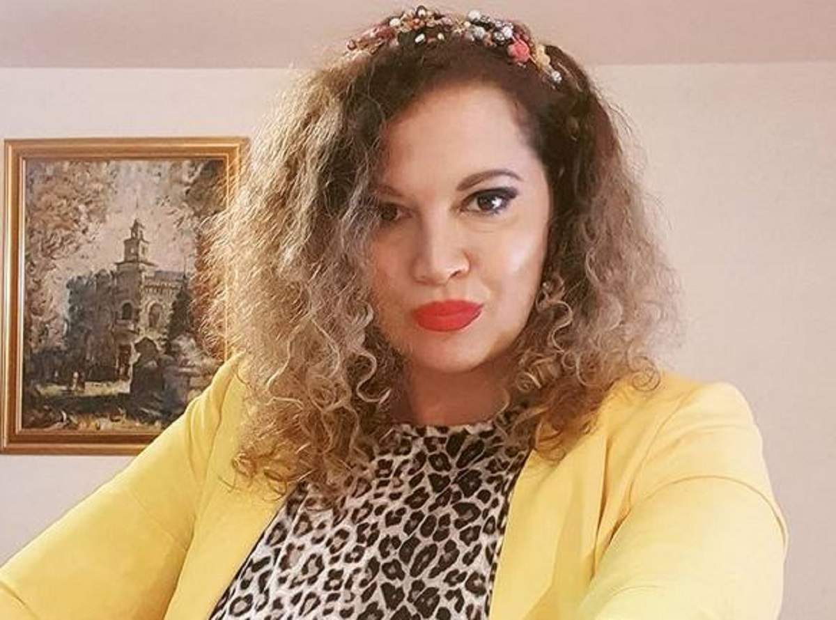 Oana Lis poartă o bluză cu animal print, stil leopard. Vedeta are pe deasupra o bluză descheiată galbenă. În spatele ei se vede un tablou pe perete.