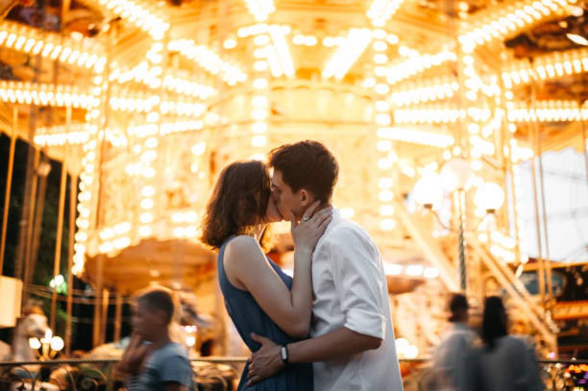 Imagine cu doi tineri intr-un parc de distractii care se saruta