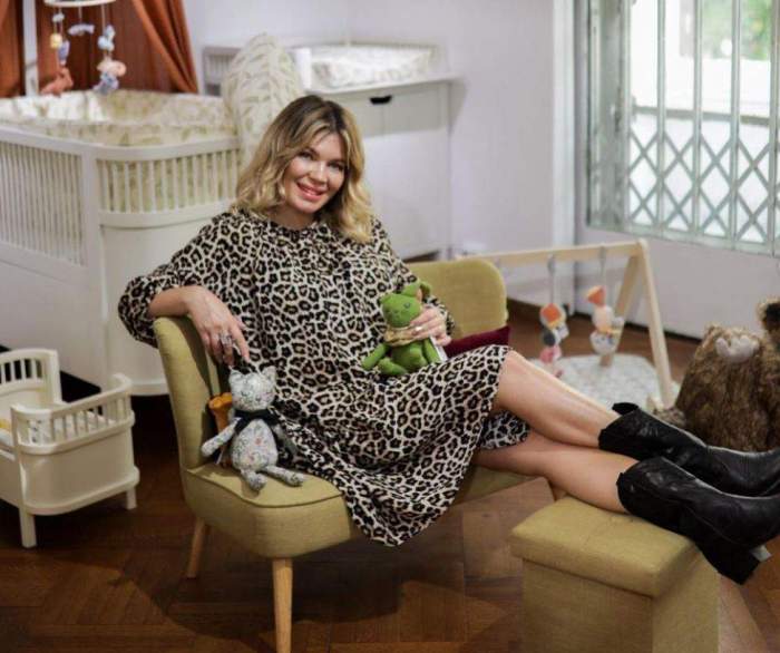 Gina Pistol, în ținută aniamal print, așezată pe fotoliu, lângă pătuțul fetiței