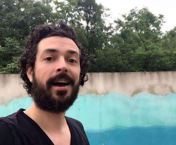 Marius Moga își face un selfie. Artistul poartă un tricou negru și ține gura deschisă.