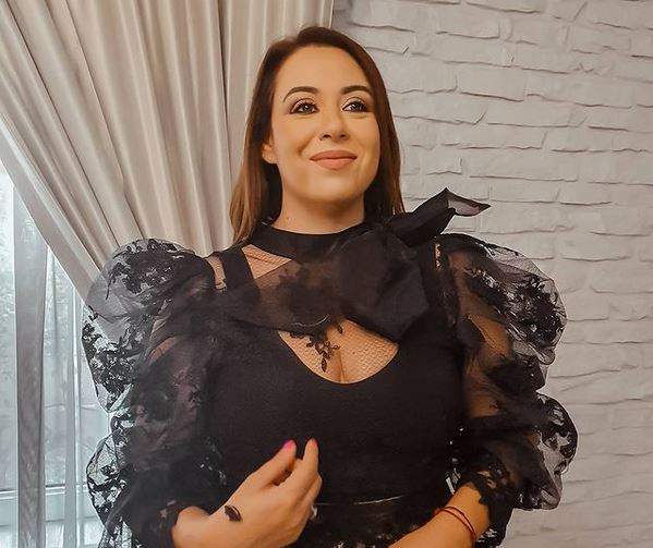 Oana Roman e îmbrăcată într-o bluză neagră cu mâneci voluminoase, transparente, cu model floral. Vedeta zâmbește.