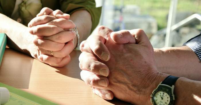 Imagine cu doua persoane care isi tin mainile incrucisate sa se roage