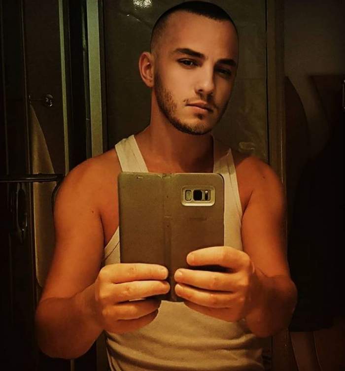 Mihai Trăistariu se află în baie și poartă un maiou alb. Artistul își face poză cu telefonul în oglindă.