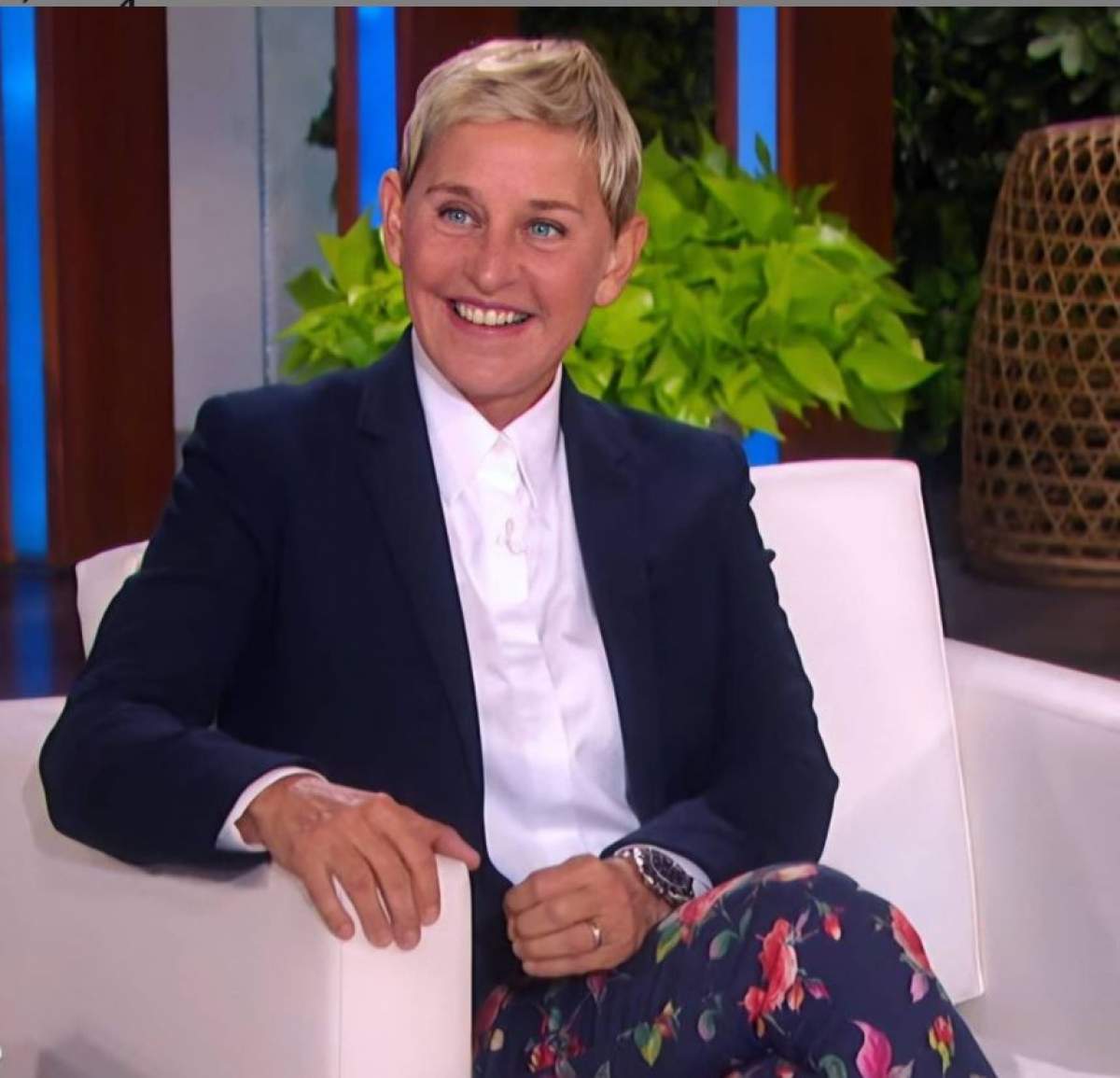Ellen DeGeneres este pe fotoliu in emisiunea ei, zambeste, are sacou negru si camasa alba