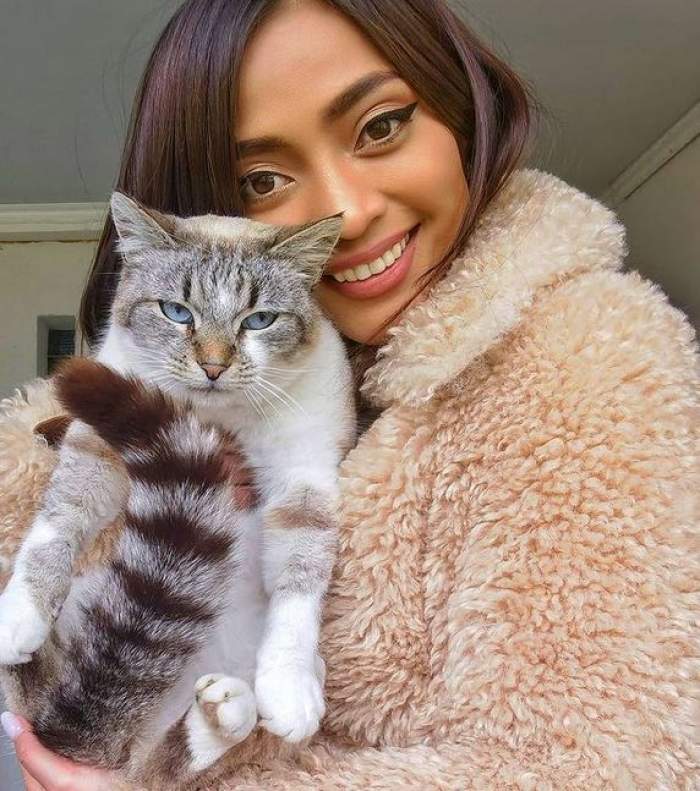 Bella Santiago poartă o haină crem, pufoasă, și-și ține în brațe pisica