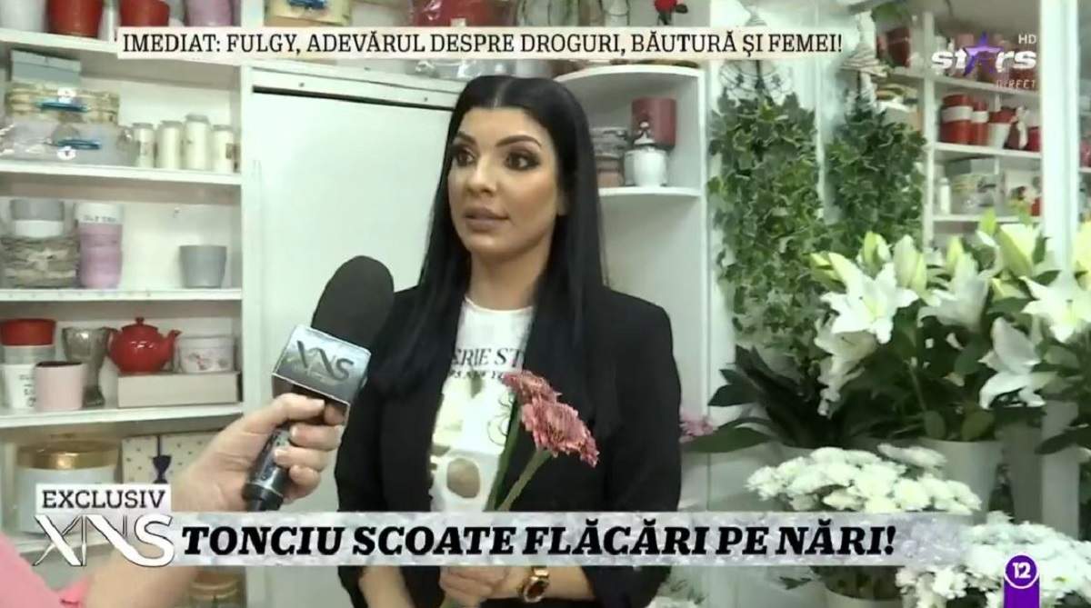 Andreea Tonciu dă un interviu la Xtra Night Show din florărie. Vedeta poartă un tricou alb și pe deasupra sacou negru.