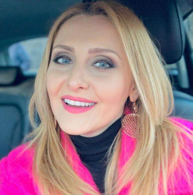 Alina Sorescu își face un selfie din mașină, purtând o maletă neagră și bluză deschieată roz.