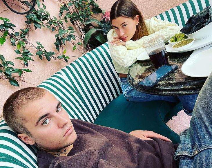 Justin Bieber își face un selfie de la o terasă, în care apare și soția lui, Hailey. Artistl are părul scurt și poartă o bluză neagră.