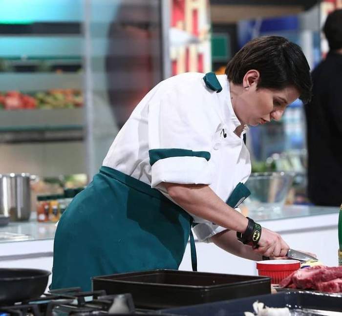 Cristina Mălai gătește la Chefi la cuțite, purtând uniformă albă de bucătar și șorț verde.