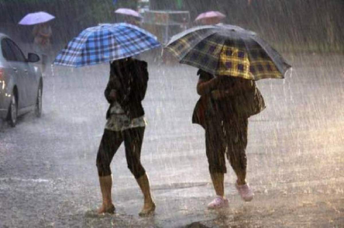 Două femei merg pe stradă și se apără de ploaie cu umbrelele. În spatele lor se vede o mașină.