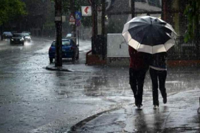 Un cuplu merge pe stradă, prin ploaie. Aceștia țin deasupra capului o umbrelă.