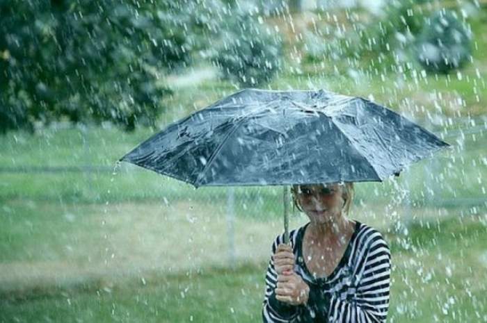 O fetiță merge prin parc și se ferește de ploaie cu umbrela.