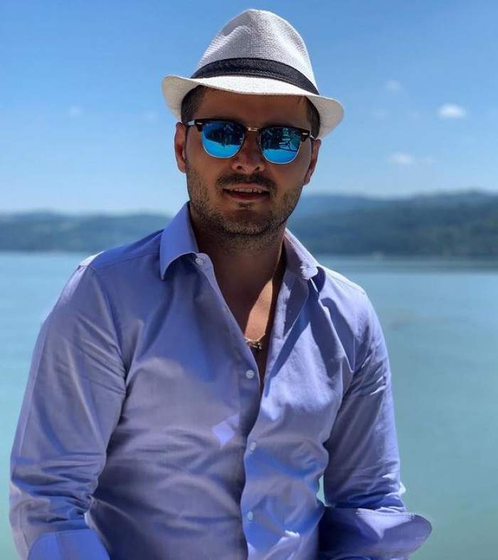 Liviu Vârciu se află la mare. Artistul poartă o pereche de ochelari de soare, o pălărie albă cu dungă neagră și o cămașă bleu.