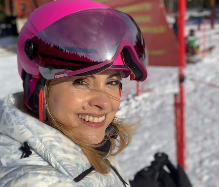 Simona Gherghe e la munte. Vedeta poartă geacă albă și o cască de protecție roz. Aceasta zâmnește larg și își face un selfie.