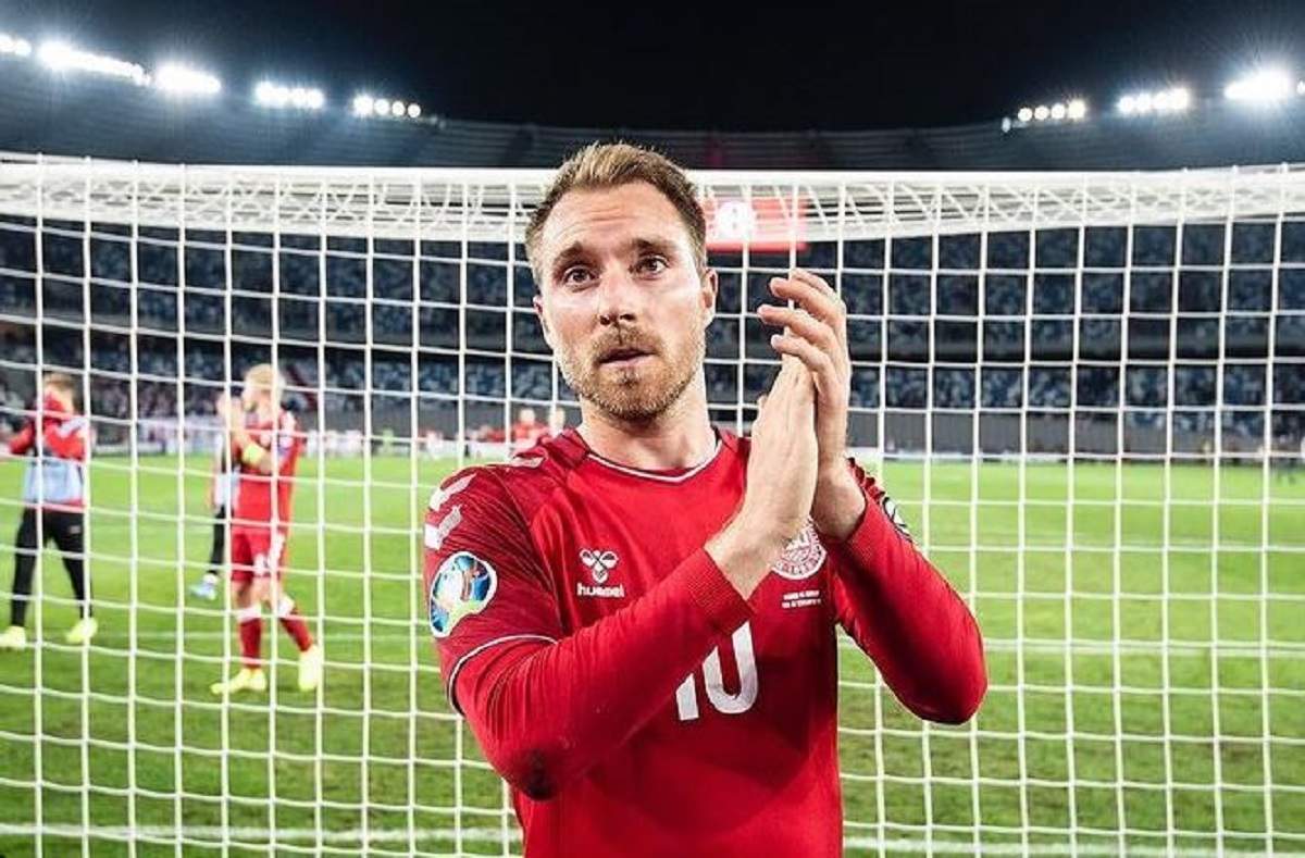 Christian Eriksen este pe terenul de fotbal, în fața porții. Fotbalistul aplaudă și e îmbrăcat în roșu.