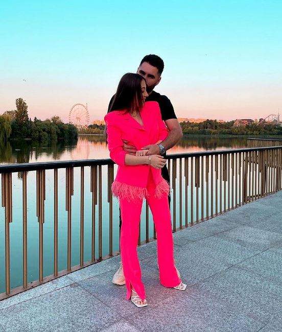 Nicole Cherry și iubitul ei sunt lângă un lac. Vedeta poartă costum roz și e ținută în brațe pe la spate de el.