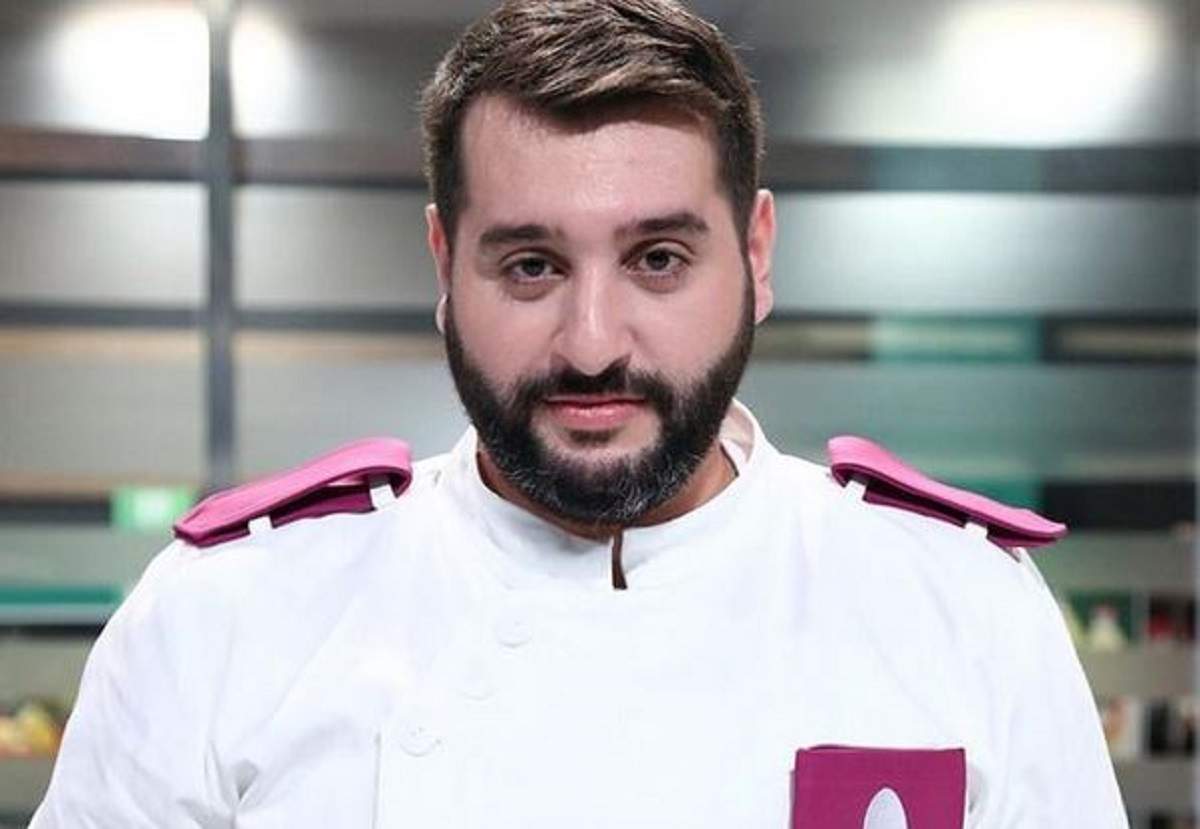 Enzo de la Chefi la cuțite poartă uniformă albă de bucătar cu detalii mov. Acesta zâmbește discret.