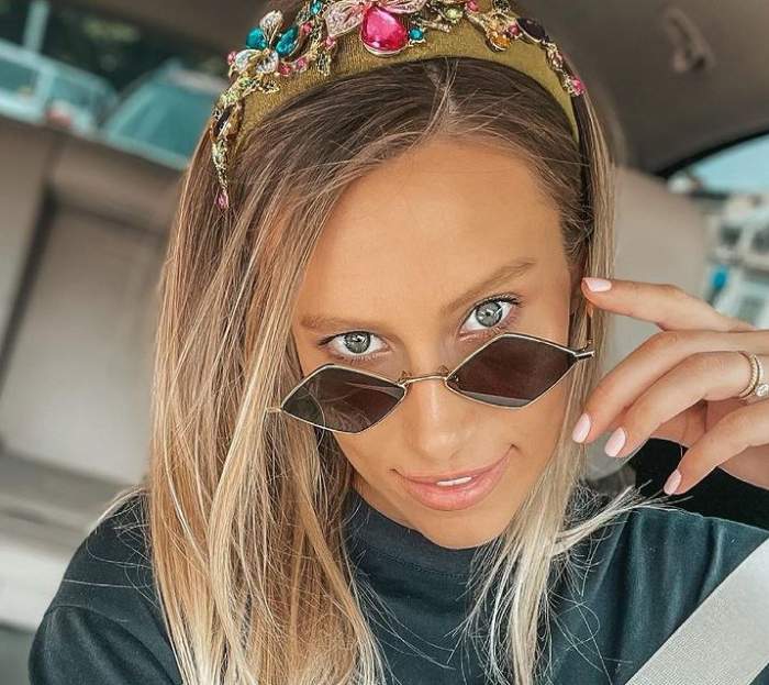 Gabriela Prisăcariu poartă ochelari de soare, tricou negru și diademă cu pietre colorate pe cap. Vedeta zâmbește și e în mașină.