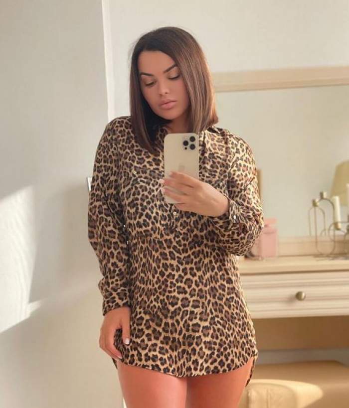 Carmen de la Sălciua are părul scurt, stă în picioare și își face o poză cu telefonul mobil, în oglindă, fiind îmbrăcată într-o rochie tip cămașă cu animal print.