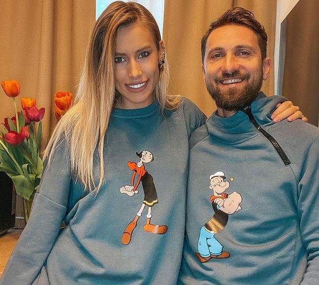 Gabriela Prisăcariu și Dani Oțil poartă amândoi bluze gri. Aceștia zâmbesc și în spatele lor se văd niște lalele în vază.