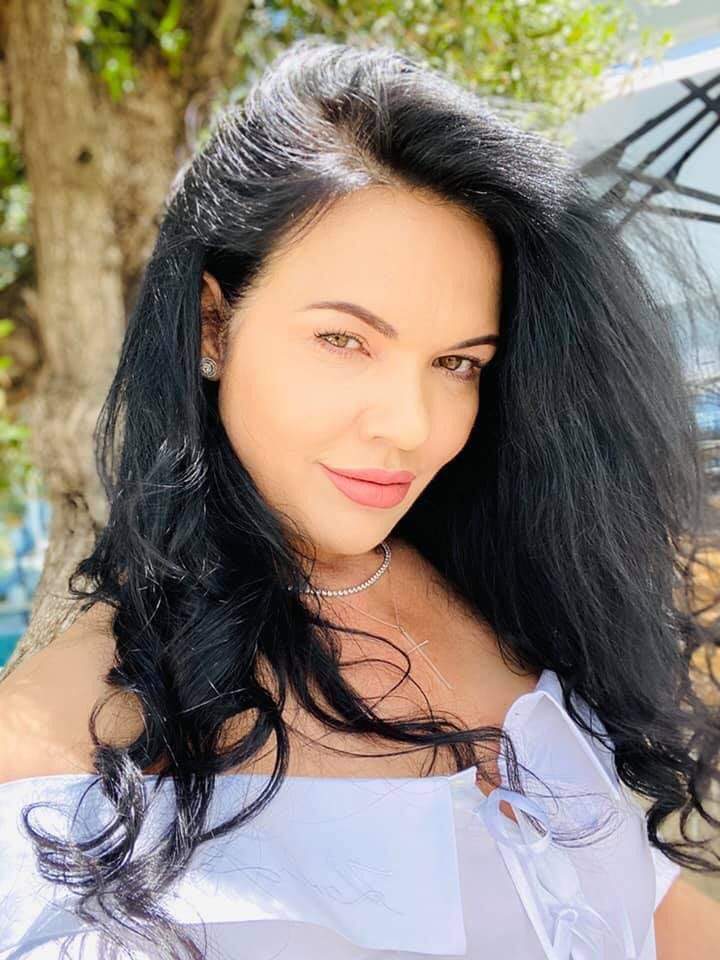 Ioana Simion își face un selfie, poartă cămașă albă și zâmbește slab.