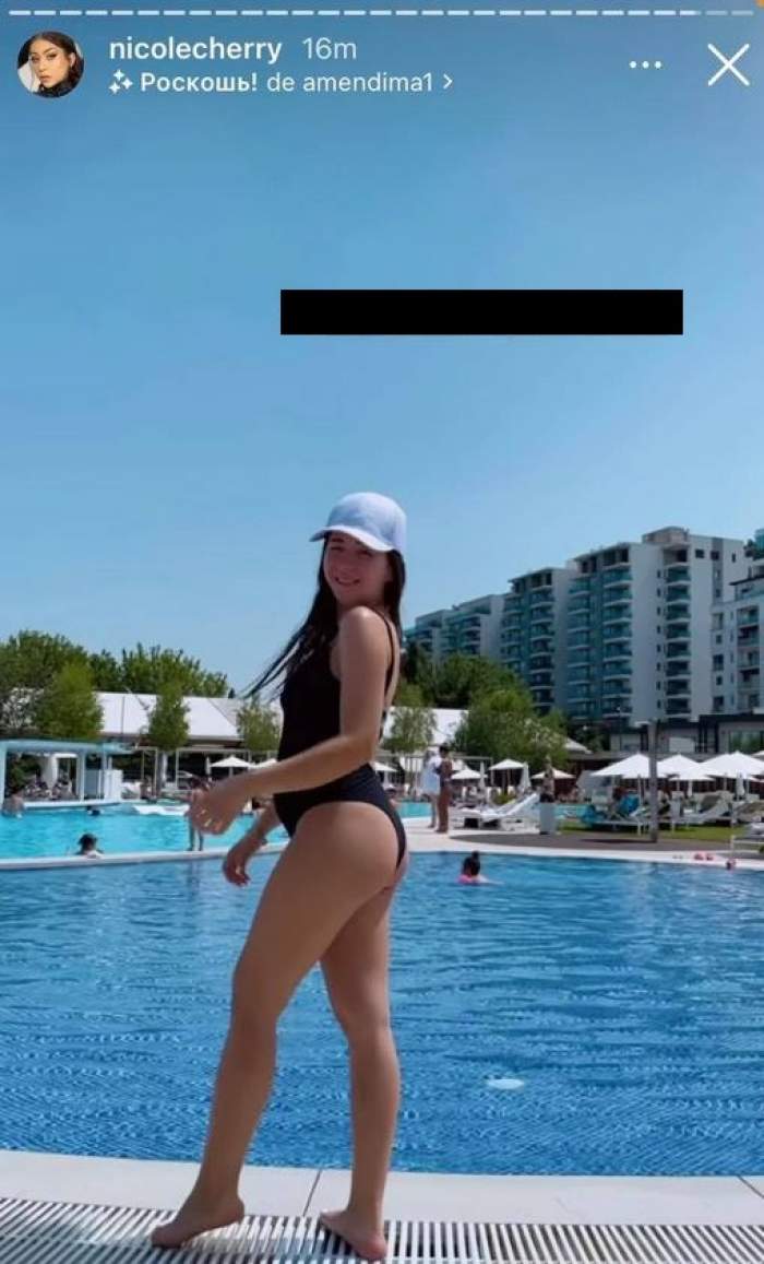 Nicole Cherry e pe marginea piscinei. Vedeta poartă costum de baie negru și șapcă albă.