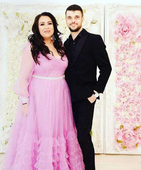 Oana Roman și Marius Elisei sunt la un eveniment. Ea poartă rochie roz, iar el costum negru și zâmbesc.