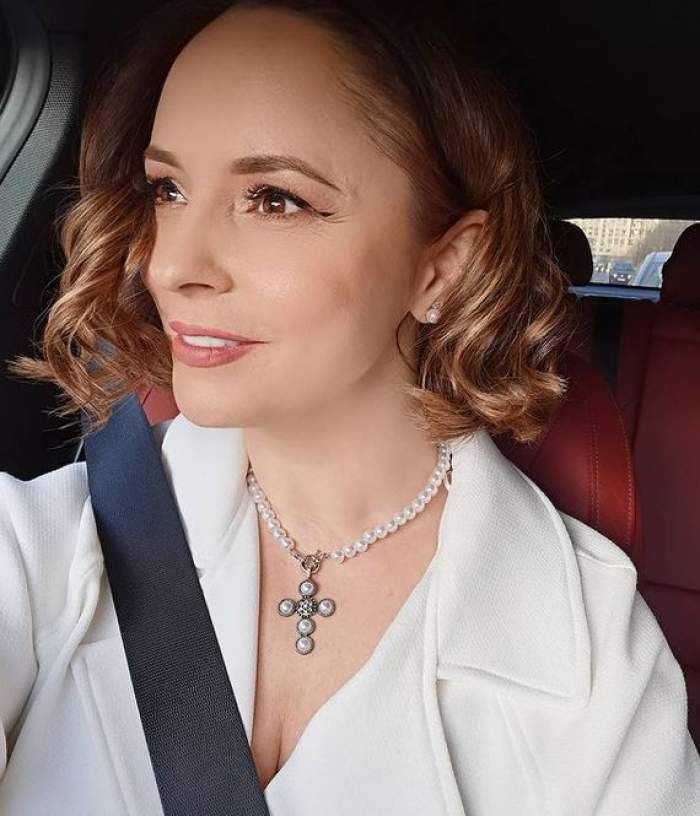 Andreea Marin își face un selfie din mașină, zâmbind. Vedeta poartă palton alb și centura de siguranță.