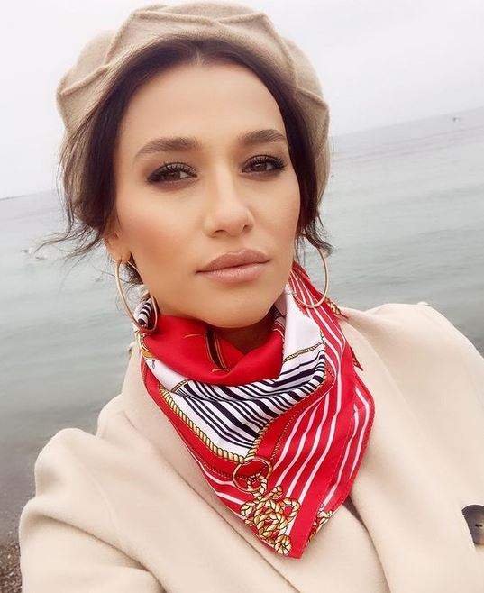 Claudia Pătrășcanu e la mare. Vedeta poartă o beretă crem pe cap. Artista e îmbrăcată cu un palton crem și are la gât o eșarfă roșie cu alb, nengru și auriu.