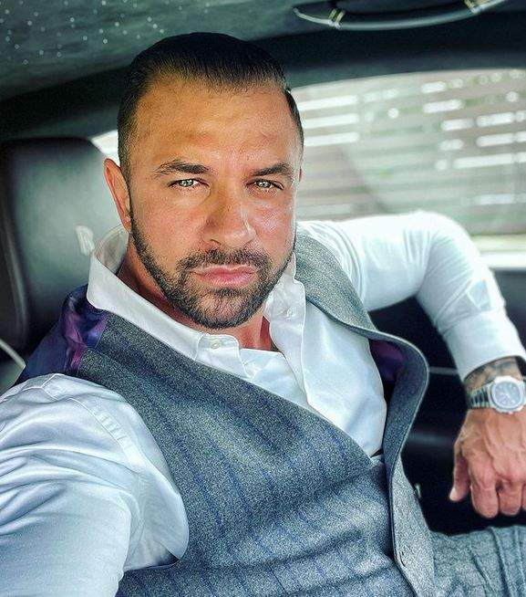 Alex Bodi își face un selfie din mașină, poartă cămașă albă și vestă gri.
