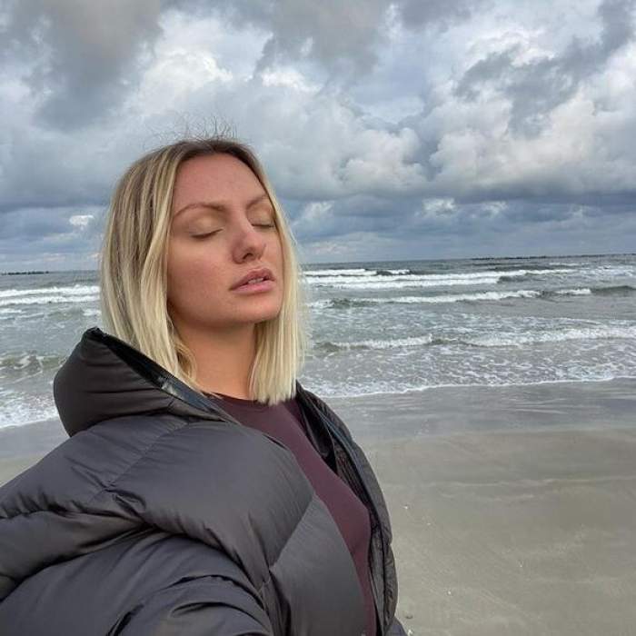 Alexandra Stan e la mare, pe plajă. Vedeta ține ochii închiși și poartă geacă neagră de iarnă.