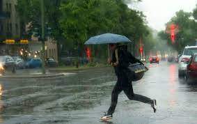O femeie care traversează strada cu umbrela în mână
