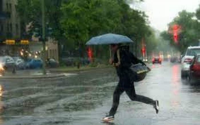 O femeie care traversează strada cu umbrela în mână