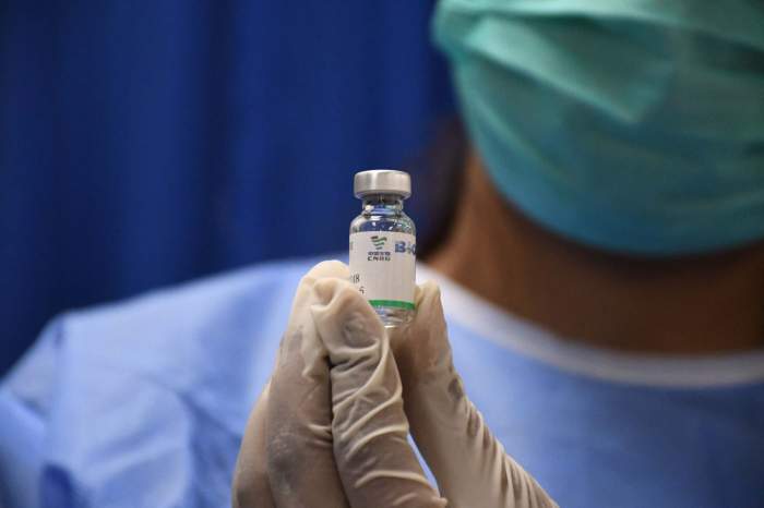 Un medic cu mască pe față, ține o sticlă de vaccin în mână