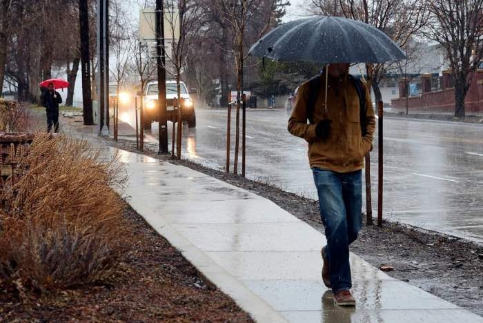 Un bărbat care merge cu umbrela în mână, pe trotuar, plouă
