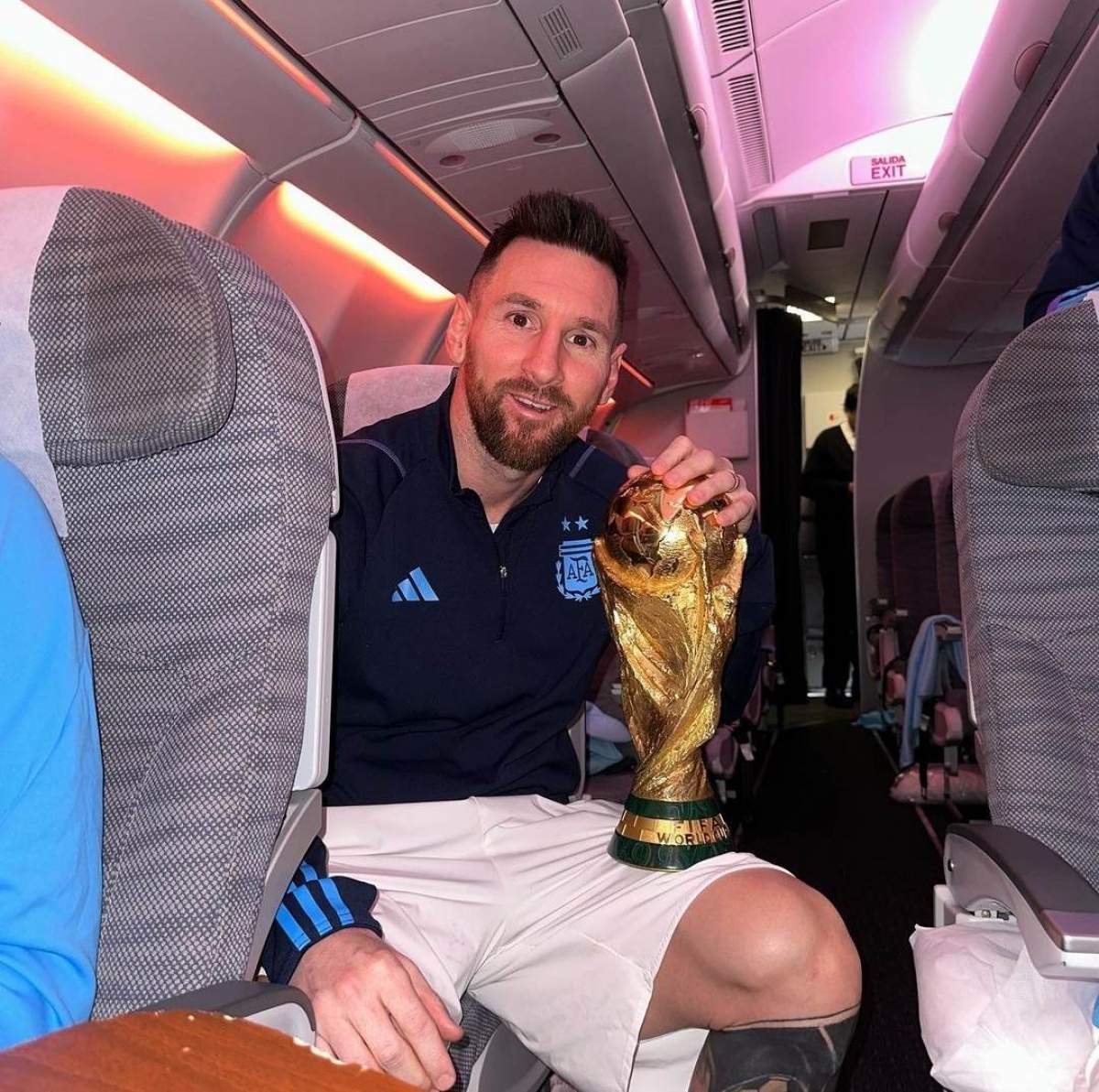 Lionel Messi în avion, împreună cu trofeul Cupei Mondiale 2022.