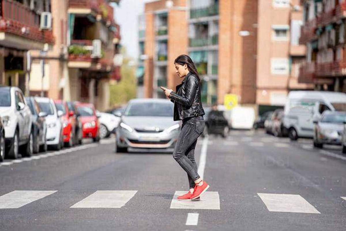 O femeie care se uită pe telefon cand traversează strada pe trecerea de pietoni