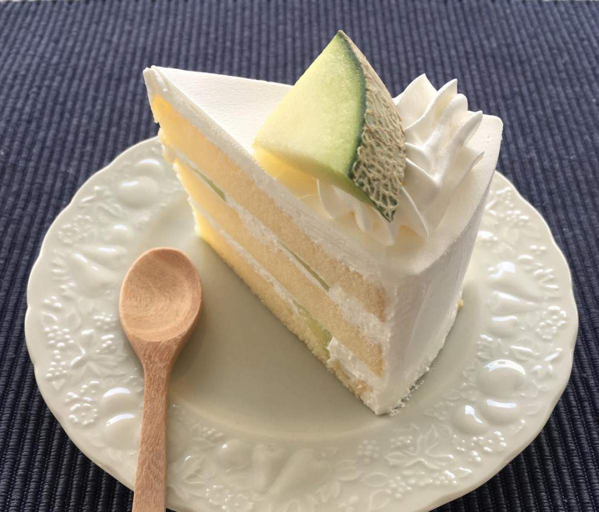 O felie de tort de pepene galben pe o farfurie alba lângă o lingură de lemn O felie de tort de pepene galben pe o farfurie alba