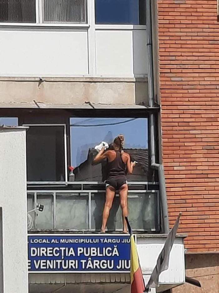 Fotografia care a devenit virală în România. O femeie îmbrăcată provocator șterge geamul unui apartament, situat deasupra unei instituții publice